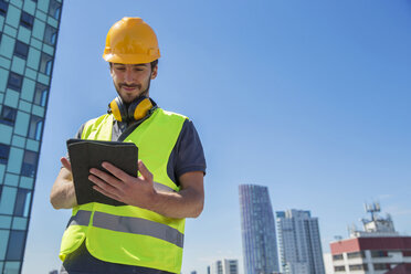 Man wearing hard hat and hi vis vest, outdoors, using digital tablet - ISF04851