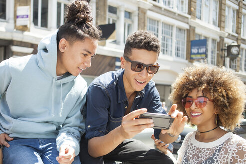 Drei junge Freunde im Freien, die auf ihr Smartphone schauen - ISF04866