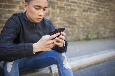 Junger Mann sitzt im Freien und benutzt sein Smartphone - ISF04874