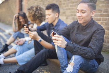 Four friends sitting in street, looking at smartphones - ISF04878