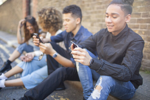 Vier Freunde sitzen auf der Straße und schauen auf ihre Smartphones - ISF04878