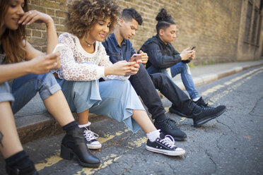 Vier Freunde sitzen auf der Straße und schauen auf ihre Smartphones - ISF04879