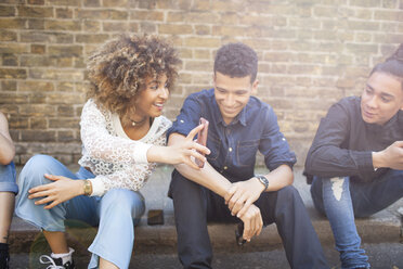 Four friends sitting in street, laughing, young woman holding smartphone - ISF04880