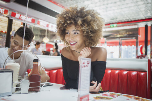Friends sitting in diner, young woman looking away, smiling - ISF04892
