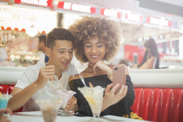Junges Paar sitzt in einem Diner, schaut auf sein Smartphone und lacht - ISF04898