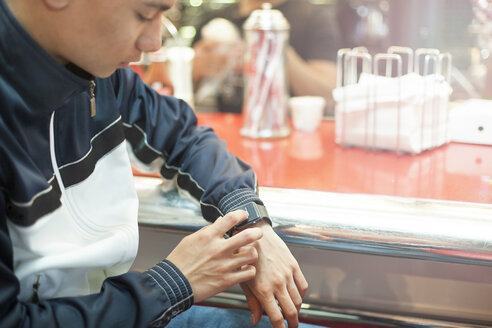 Young man sitting in diner, using smartwatch, mid section - ISF04900