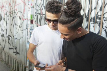 Zwei junge Männer auf der Straße, die auf ihr Smartphone schauen - ISF04905