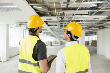 Two men wearing hi vis vest, having discussion in newly constructed office space, rear view - ISF04924