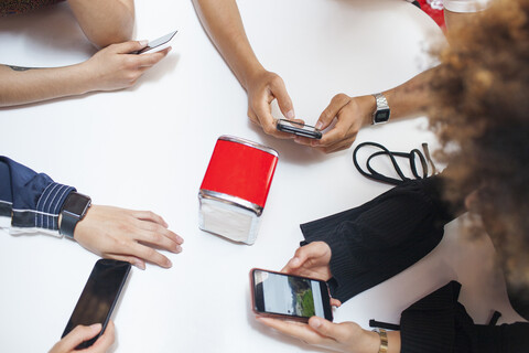 Gruppe junger Freunde, die am Tisch sitzen und Smartphones benutzen, Mittelteil, lizenzfreies Stockfoto