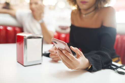 Young couple, sitting in diner, young woman using smartphone, mid section, close-up - ISF04942