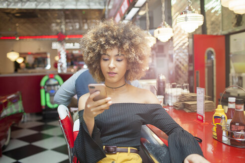 Young woman sitting in diner, looking at smartphone - ISF04944