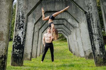 Junge Frau balanciert auf den Händen eines Mannes und praktiziert Yoga unter einer Betonbrücke - ISF04990