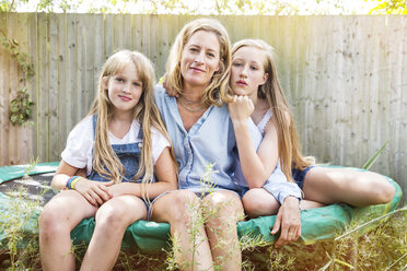 Portrait of mother and daughters sitting on trampoline looking at camera smiling - ISF04999