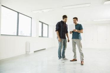Two men standing in empty office space, looking at digital tablet - ISF05020