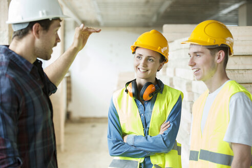Three people standing in constructions site, wearing hard hats, having discussion - ISF05021