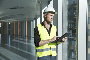 Man wearing hard hat and hi vis vest, looking at digital tablet - ISF05022