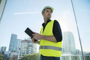 Man wearing hard hat and hi vis vest, holding digital tablet - ISF05023