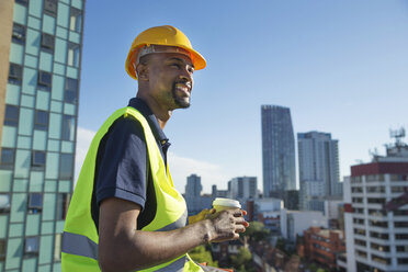 Construction worker outdoors, holding takeaway coffee cup, elevated view of surrounding buildings - ISF05025