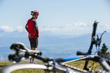 Älterer Mann mit Fahrradhelm, auf einem Hügel stehend, mit Blick auf die Landschaft, Fahrrad im Vordergrund - ISF05027