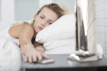 Young woman in bed, reaching for smartphone on bedside table - ISF05031