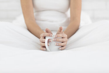 Junge Frau im Bett sitzend, Tasse Kaffee in der Hand, Mittelteil - ISF05037