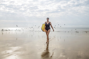 Woman carrying surfboard on beach, Folkestone, UK - ISF05044