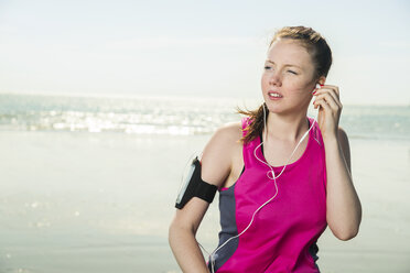 Junge Frau mit Kopfhörern am Strand, die Musik auf einer Armbinde einstellt, Folkestone, UK - ISF05052