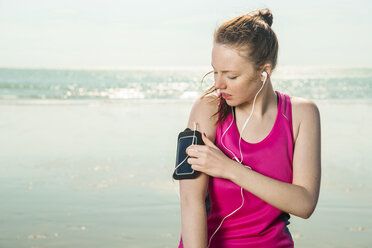 Junge Frau mit Kopfhörern am Strand, die Musik auf einer Armbinde einstellt, Folkestone, UK - ISF05061