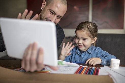 Man and daughter at table waving at digital tablet - ISF05074