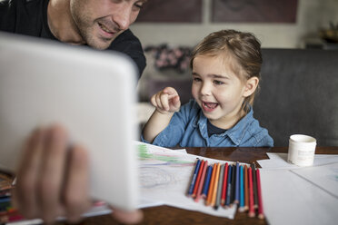 Mann mit Tochter am Tisch, der auf ein digitales Tablet zeigt - ISF05075