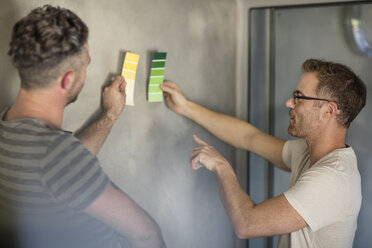 Zwei Männer halten Farbmuster an eine kahle Wand - ISF05090