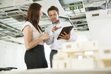 Businessman and woman having discussion, looking at digital table, architectural model on tablet, low angle view - ISF05099