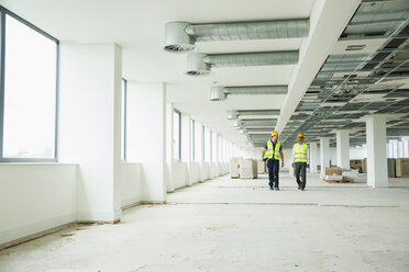 Zwei Arbeiter mit Warnwesten gehen durch einen neu errichteten Büroraum - ISF05100
