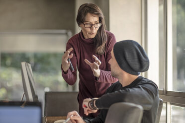 Eine Geschäftsfrau erklärt einem jungen männlichen Designer am Schreibtisch zu Hause etwas - ISF05123