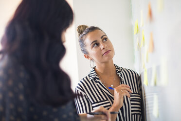 Junge Geschäftsfrauen mit Blick auf Whiteboard-Haftnotizen - ISF05171