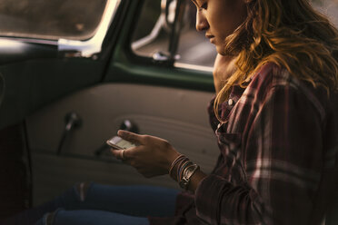 Junge Frau schaut auf ihr Smartphone auf dem Vordersitz eines Pickups in Newport Beach, Kalifornien, USA - ISF05182