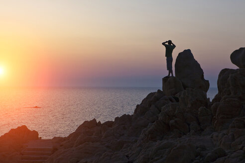 Silhouette eines Mannes auf einem Felsen mit Blick auf den Sonnenuntergang über dem Meer, Olbia, Sardinien, Italien - ISF05201