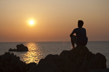 Silhouette eines Mannes auf einem Felsen mit Blick auf den Sonnenuntergang über dem Meer, Olbia, Sardinien, Italien - ISF05225