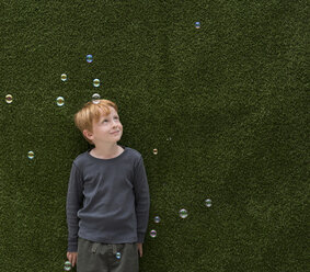 Boy in front of artificial grass smiling at bubbles - ISF05280