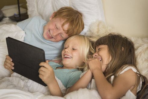 Children lying in bed looking at digital tablet - ISF05283