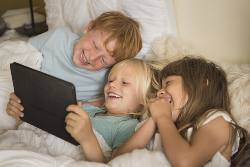 Kinder liegen im Bett und schauen auf ein digitales Tablet - ISF05283