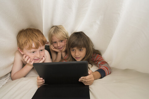 Kinder liegen im Bett und schauen auf ein digitales Tablet, lizenzfreies Stockfoto