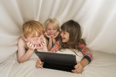 Children lying in bed looking at digital tablet - ISF05285