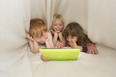 Children lying in bed looking at digital tablet - ISF05286