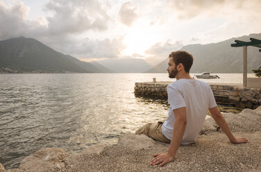 Junger Mann sitzt am Wasser und schaut weg, Kotor, Montenegro, Europa - ISF05519