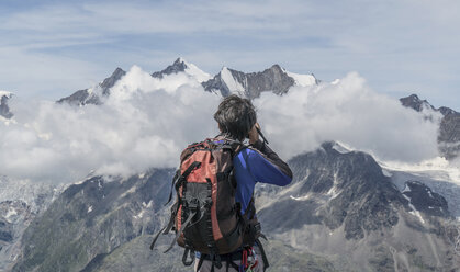 Rear view of male climber photographing low mountain clouds at Jegihorn, Valais, Switzerland - ISF05690