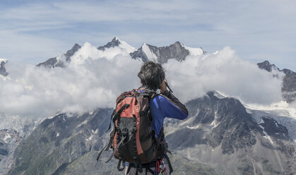 Rückansicht eines männlichen Bergsteigers beim Fotografieren tiefer Bergwolken am Jegihorn, Wallis, Schweiz - ISF05690