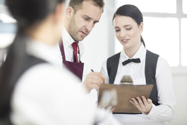 Waiting staff in restaurant, waiter writing on clipboard - ISF05724