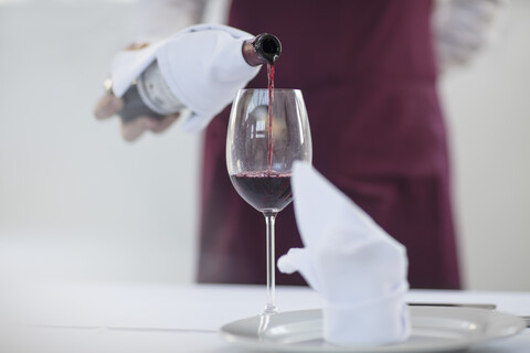 Kellner in einem Restaurant, der ein Glas Rotwein einschenkt, Mittelteil, lizenzfreies Stockfoto