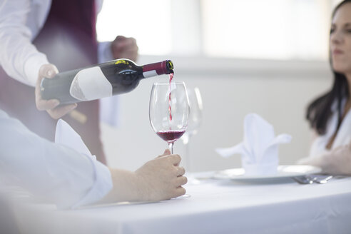 Waiter in restaurant, pouring wine for diners, mid section - ISF05734